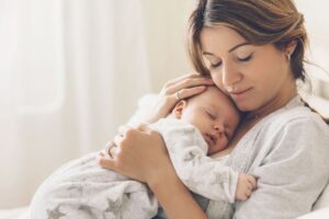 new mom sitting with baby on her chest, both wearing white and grey